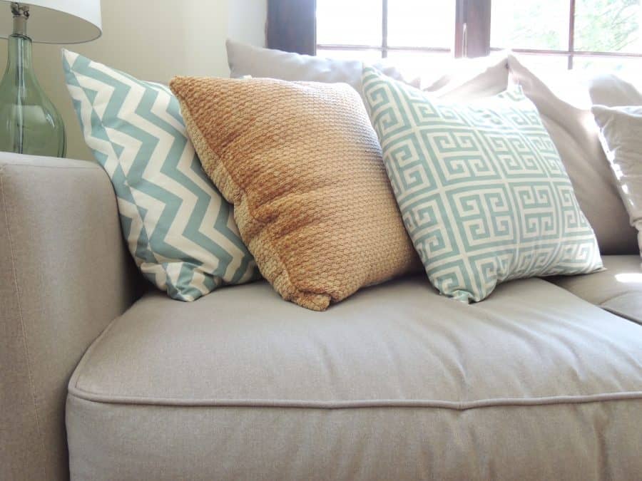 Three throw pillows rest on a light grey sofa below a window
