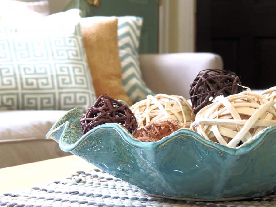 A wavy, blue, glass container holding decorative rattan balls on a coffee table