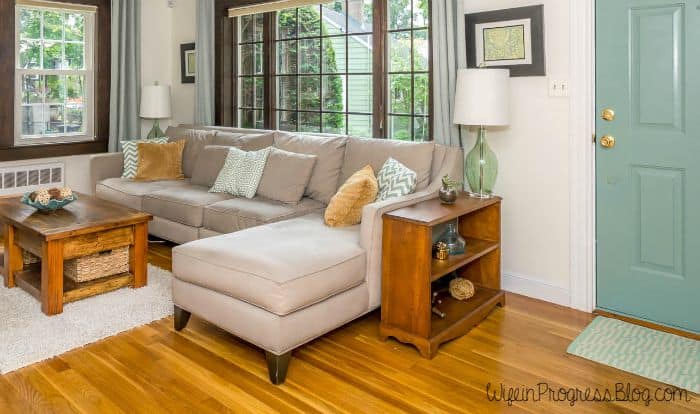 The chaise lounge portion of the sofa, near a 2-shelf book stand and a lamp with a green, glass base