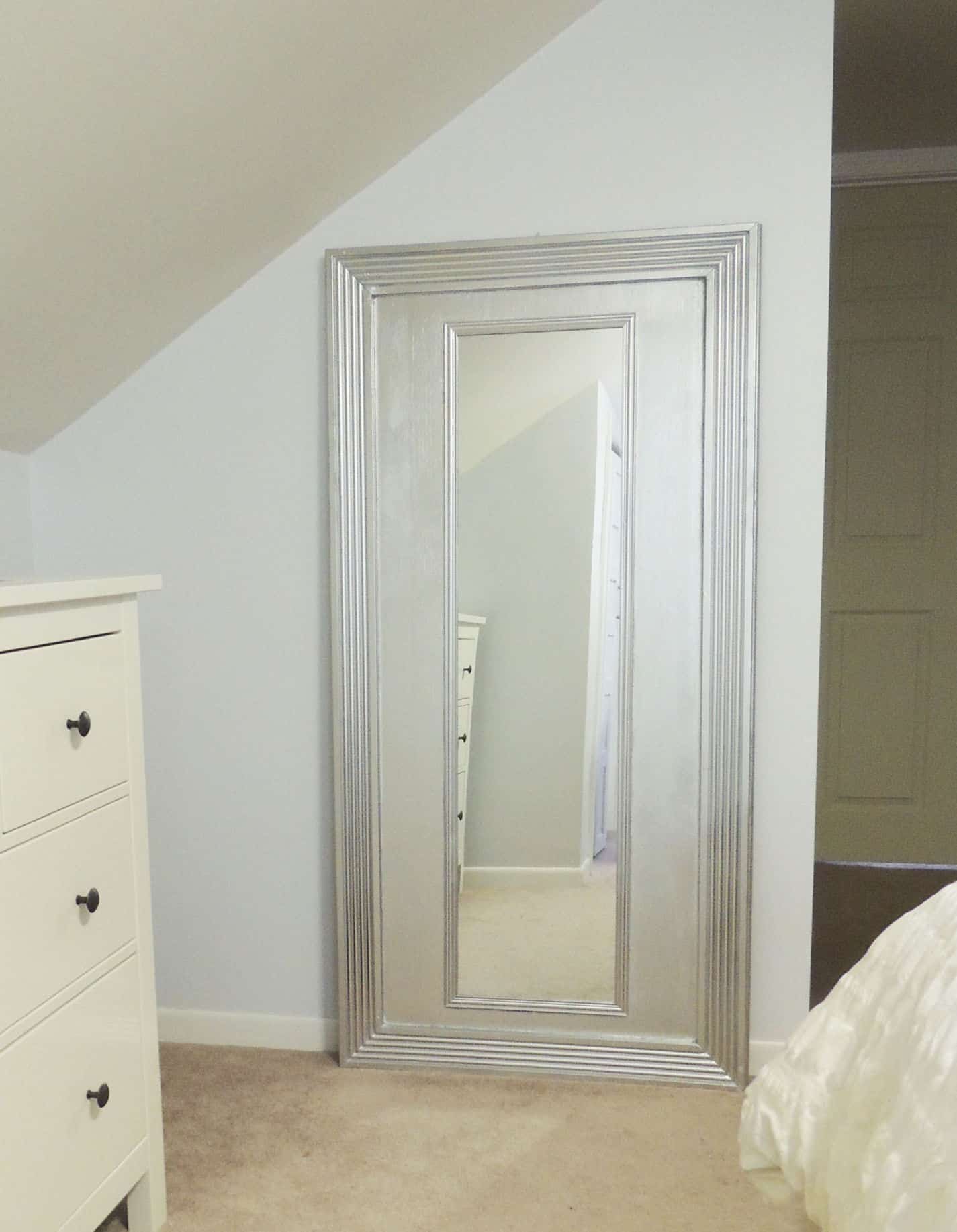 A large, floor-length silver mirror leaning against a light blue wall