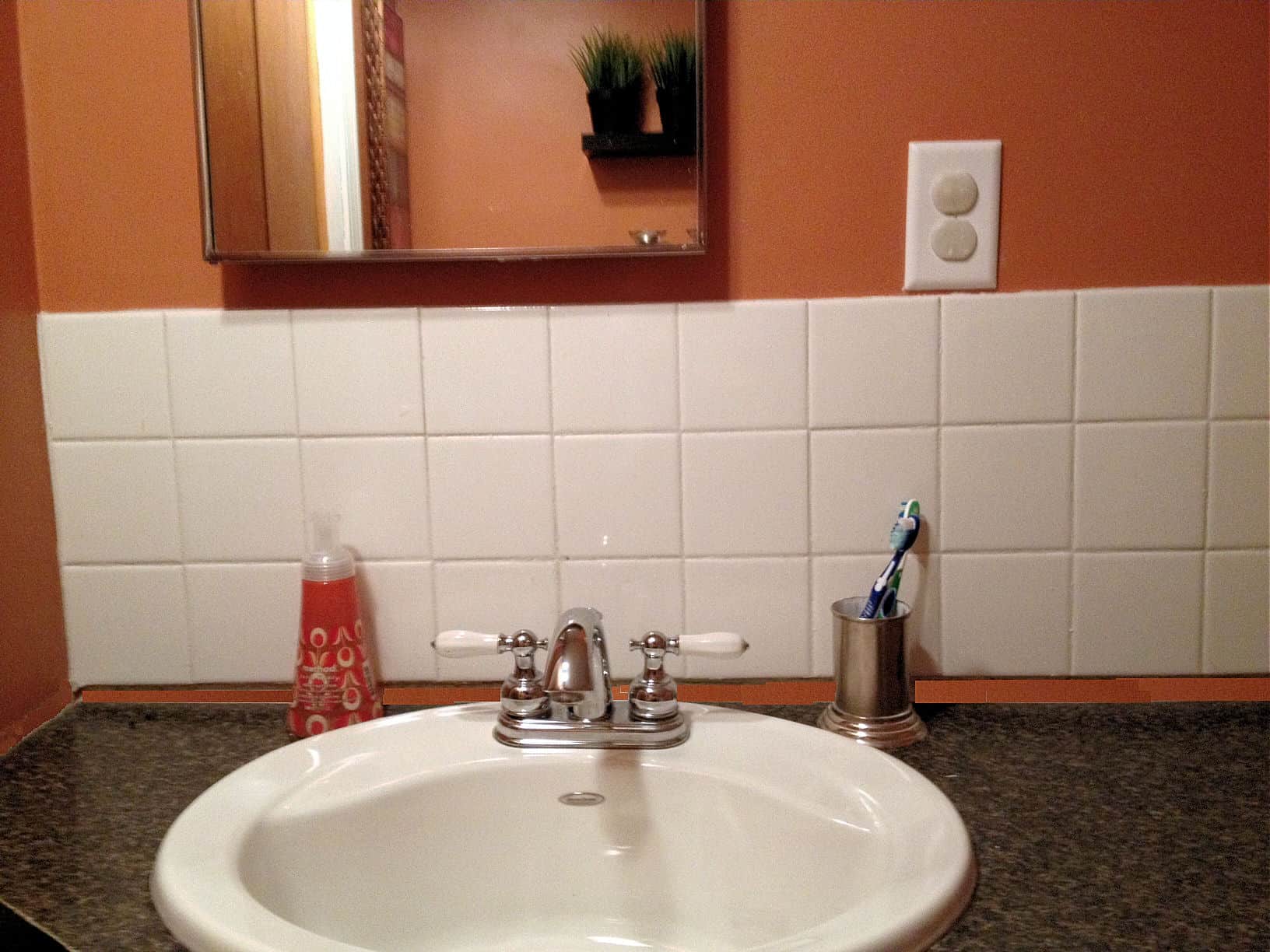 A round, white sink on dark countertop, with old-fashioned, square, white tiles above and a recessed medicine cabinet