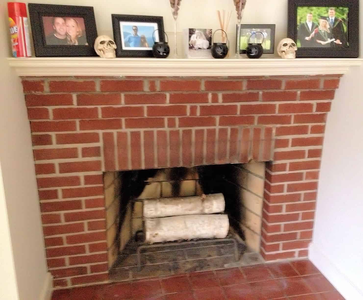 A brick fireplace and wooden mantel with photo frames and various Halloween decor