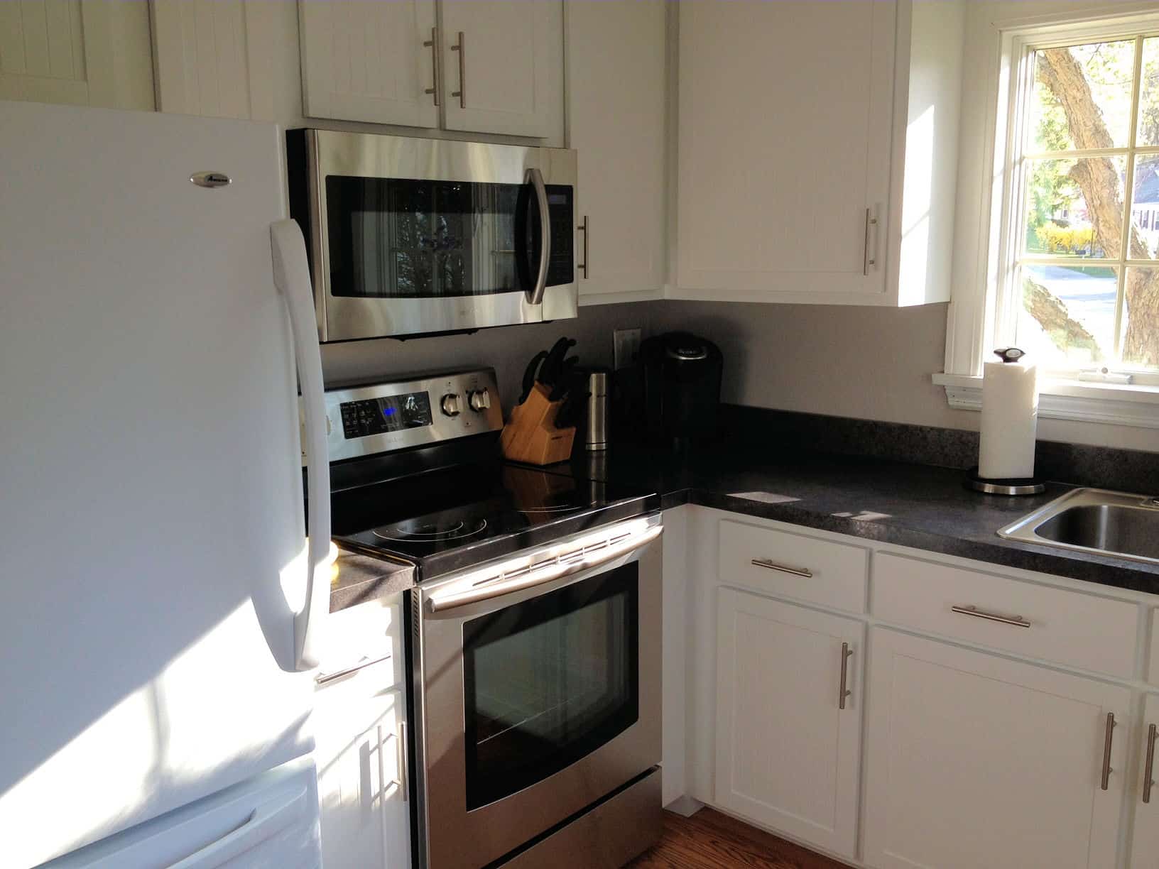 The corner of a kitchen, with white cabinets, stainless steel stove and microwave and a white fridge