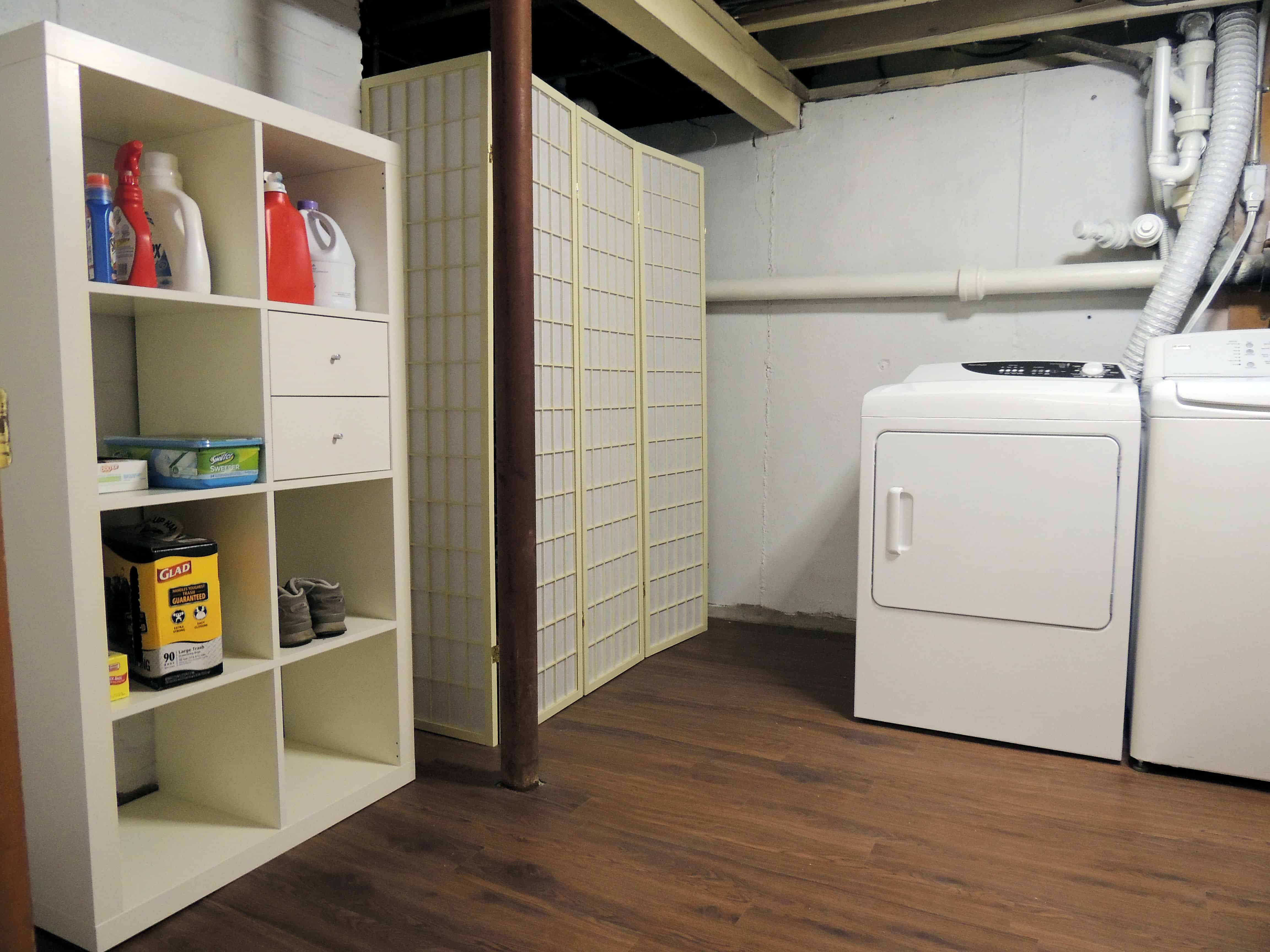 A dryer next to a screened in area and a tall shelving system with laundry supplies