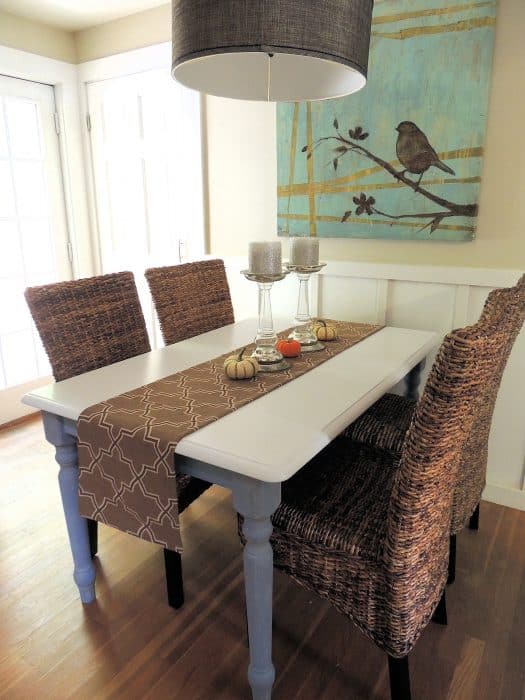 A blue and white table with a brown table runner, two glass candle holders and a trio of little pumpkins