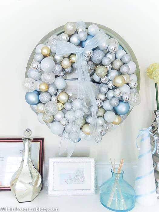 A large wreath made with light blue, silver, white and gold ornaments and a light blue, sheer ribbon