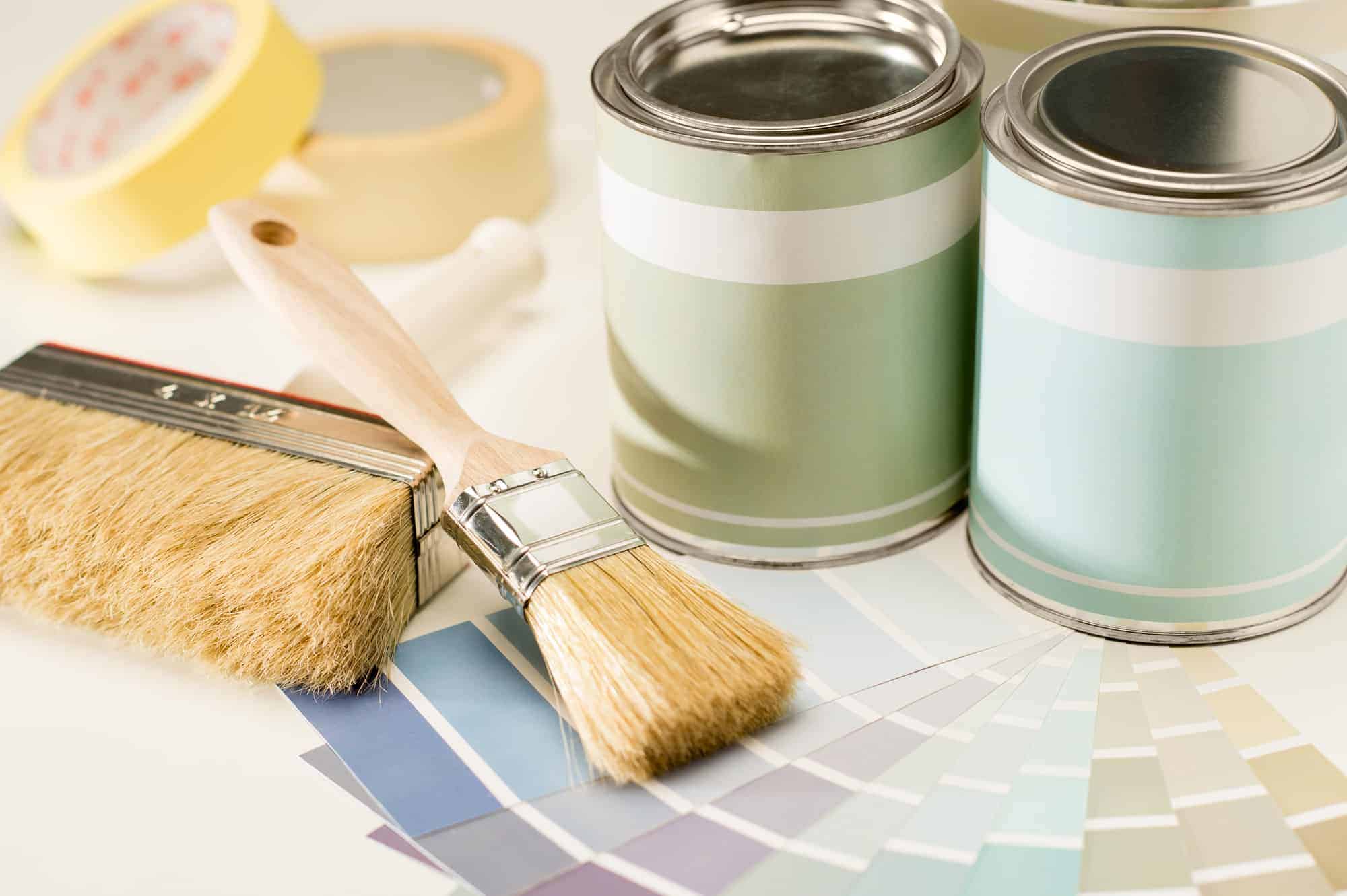 Two small cans of paint on the right; two paint brushes, some painter\'s tape and paint swatches on the left