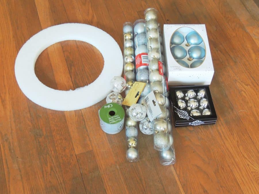 The materials laid out on a wooden floor: styrofoam wreath form, ornaments, and ribbon.