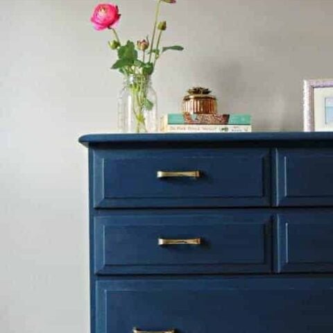 Tall dresser painted in deep blue with silver hardware, with vase of flowers resting on top