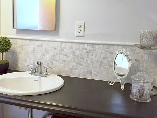 A dark countertop holding a decorative mirror, a jar of soap, and a tall, glass candle holder