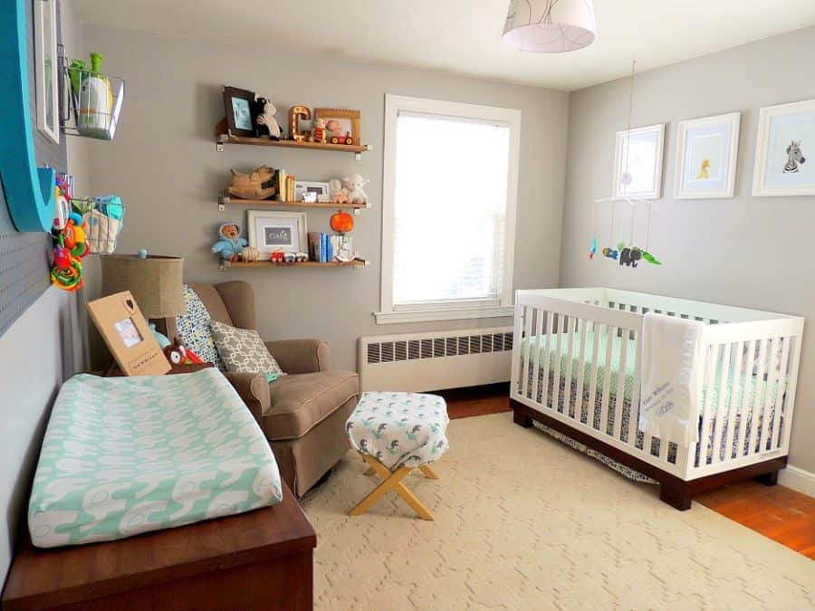 A nursery with a white crib, dark brown changing table/dresser and a few floating shelves near a window, holding various decor items