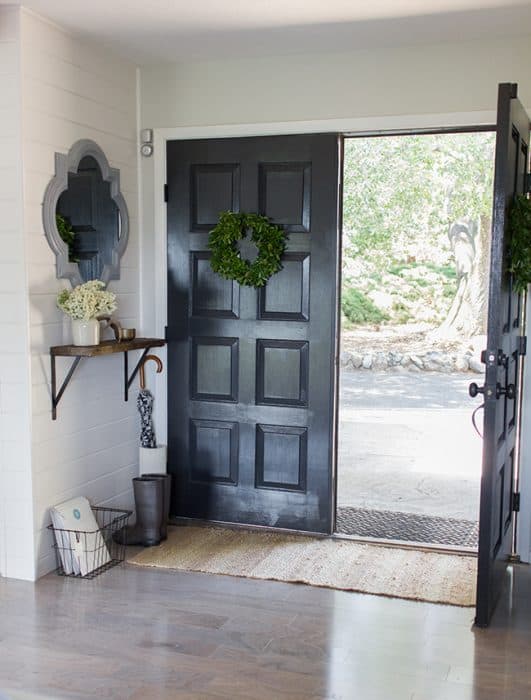 An open front door, painted black, with a shelf and mirror nearby and a long, brown rug below