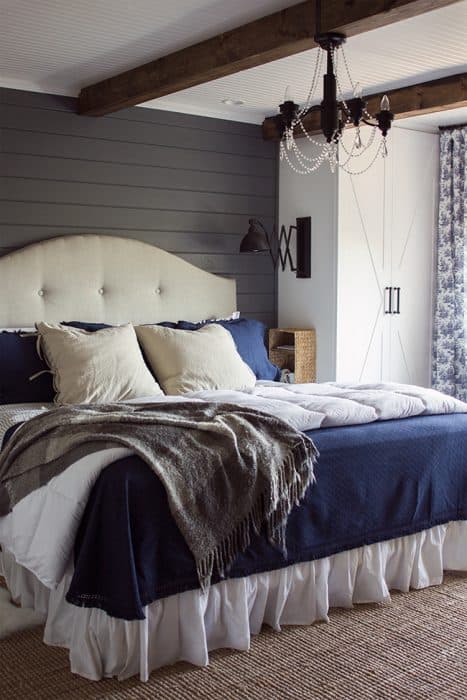 A bedroom with a large bed covered with blue, white and cream bedding, in front of an accent wall of dark grey wood planks