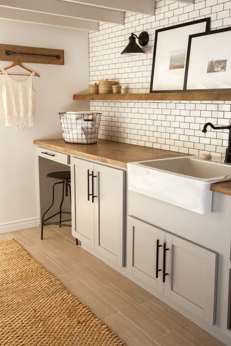 A laundry room with a sink and cabinets, a rustic wood countertop with a wire basket of towels and a long, floating shelf with artwork