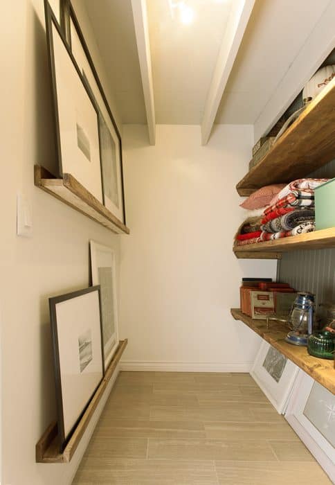 A storage room with narrow shelves on the left for artwork and deeper shelves on the right for blankets and other household items