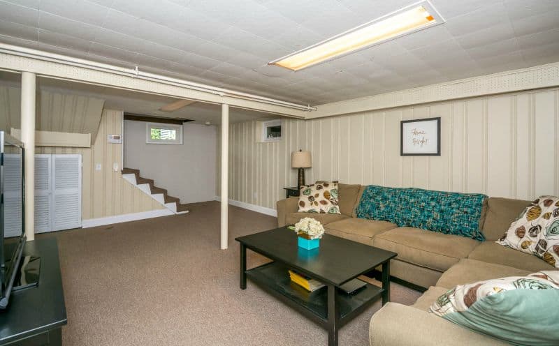 A long, grey couch with a blue throw blanket, dark coffee table and beige carpeting