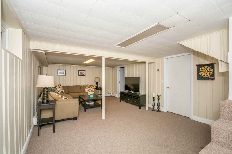 A large room in the basement with light colored, wood paneled walls, brown sofas and dark coffee table, side table and television table