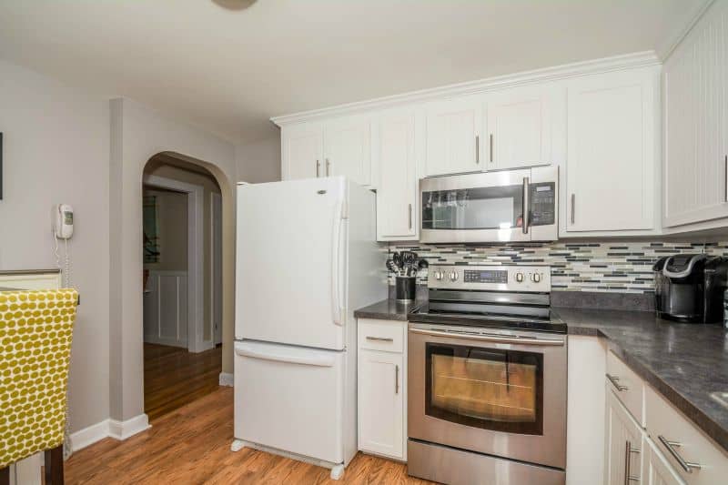A kitchen with a stainless steel stove and microwave, a white fridge and hardwood floors with a grey and white tiled backsplash