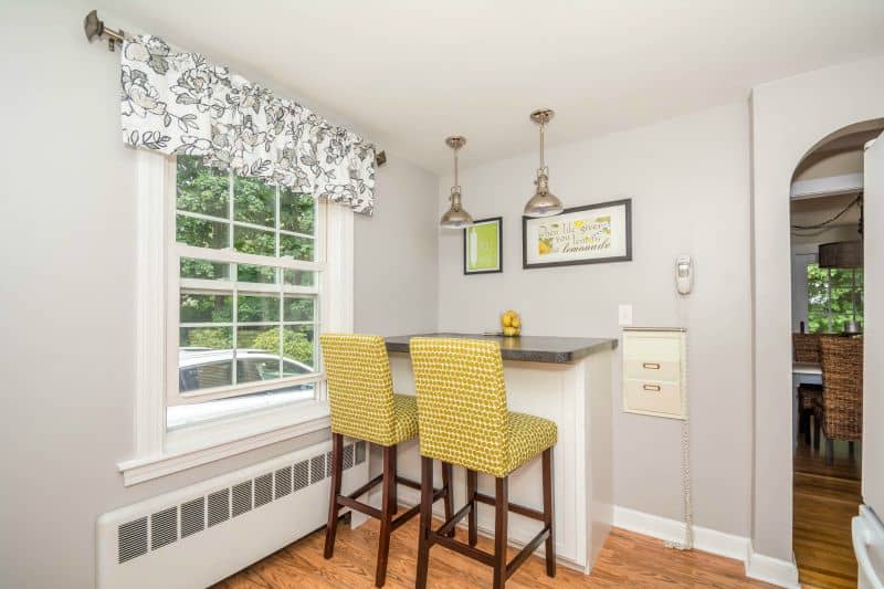 A dining nook in a kitchen with a countertop and yellow wicker chairs, counter-height, near a large window