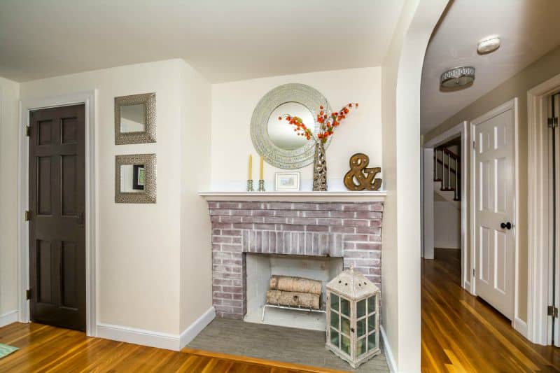 A brick fireplace with a silver mirror hung above, and various decor items on the wooden mantel