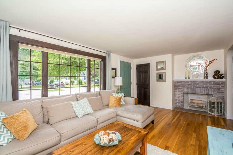 A light grey sofa set in front of a large window, with a brick fireplace in the background