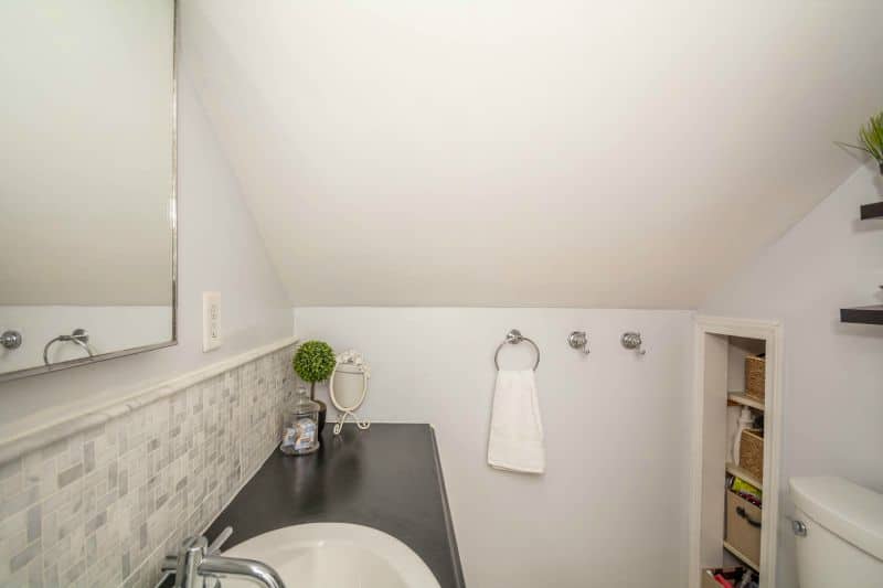 A bathroom with sloping walls, painted in light colors, with grey and white tiles above the sink area