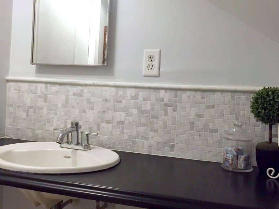 A sleek, new countertop with a new white sink, grey and white tile backsplash and light grey walls