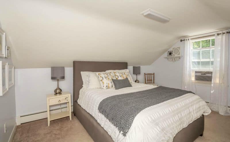 A bedroom with white and grey bedding, next to a beige nightstand