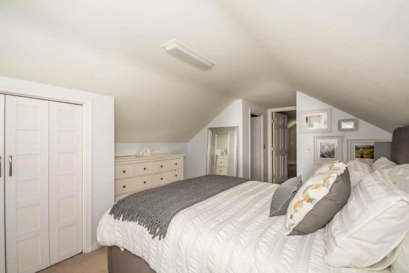 A bedroom with sloping ceilings, a beige dresser and a small closet