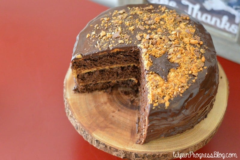 A chocolate cake resting on a rustic wood cutting, with a large slice of cake cut out