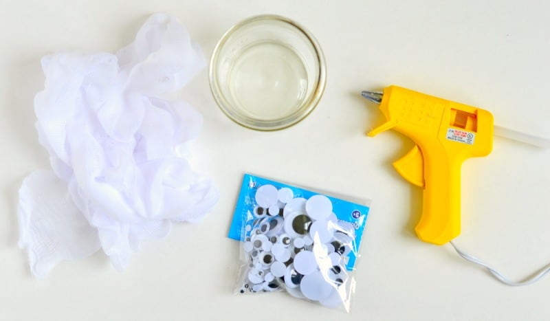 A mason jar, yellow glue gun, a package of googly craft eyes of various sizes and strips of gauze material