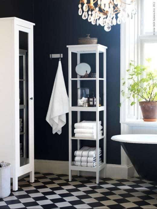 A bathroom with navy walls, white trim, checkered tile floors and white shelving and storage