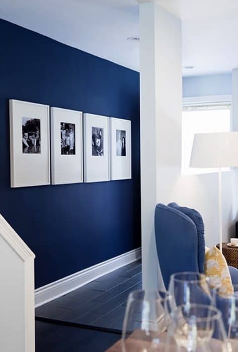A dark blue wall in a hallway with four large, white frames with black and white photographs 