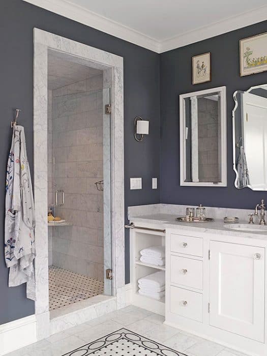 A bathroom with dark blue walls, white double sink, and a walk-in shower with glass door