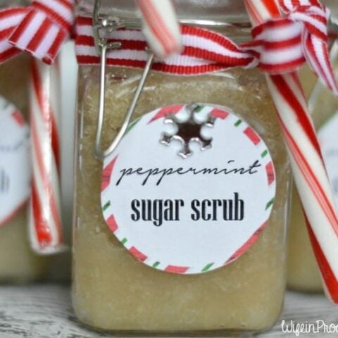 A mason jar filled with a light brown mixture of peppermint-scented sugar scrub, topped with a striped ribbon and candy cane