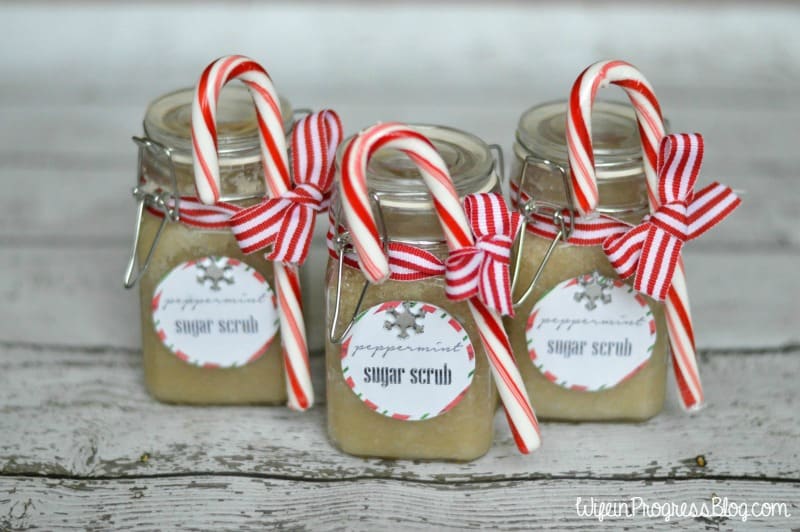 Three glass jars with covers, holding DIY peppermint sugar scrub, each decorated with a label, red and white ribbon and a candy cane