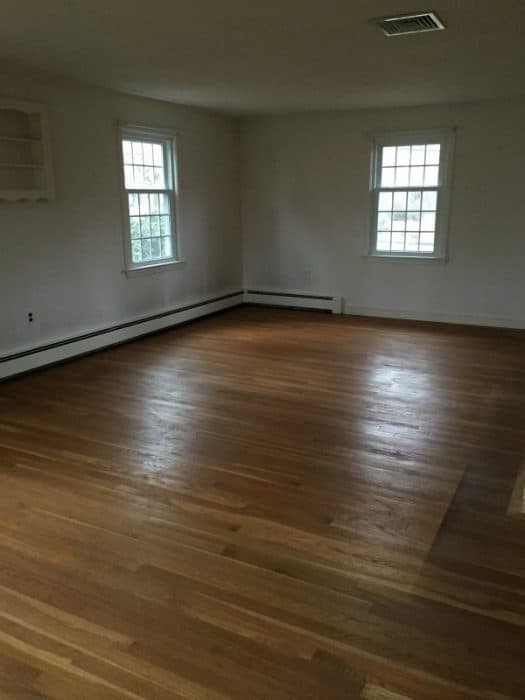 A large empty room with a hard wood floor and two windows 