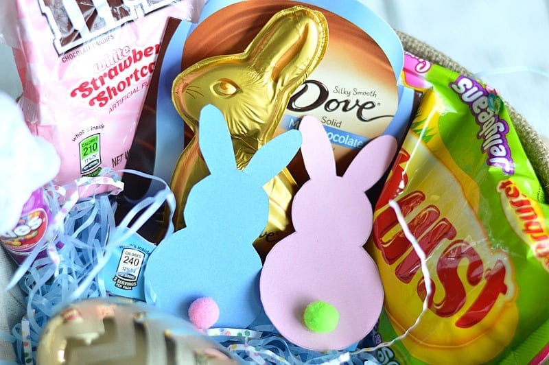 Pink and blue paper Easter bunnies with cute little pom pop tails in a basket filled with candies