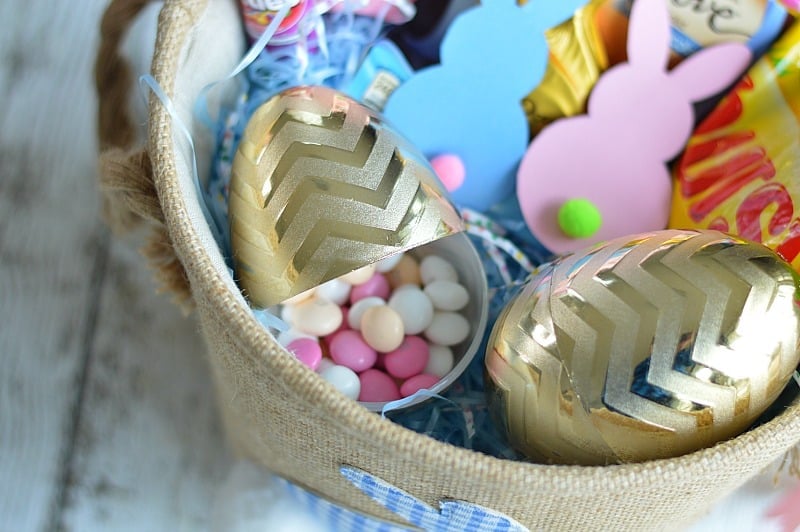 Golden chevron-patterned plastic Easter eggs, filled with pink candies, with paper bunnies nearby in canvas basket