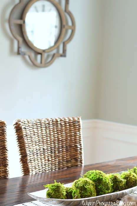 A tray of moss balls in the center of a dining table, with a large wooden clock on the wall in the background