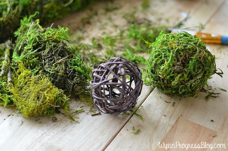 A rattan decorative ball resting on a wooden table, to be covered in moss