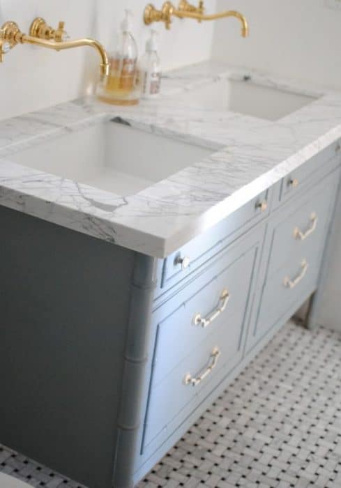 A double sink with marble countertop, blue cabinet and gold faucet and handles