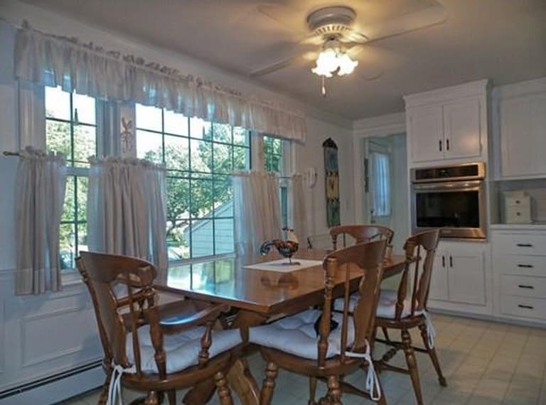 A large wooden table with matching chairs and cushions by a large window in the kitchen