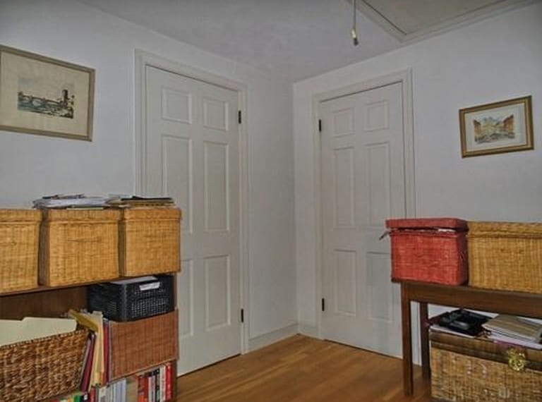The corner of a room with hardwood floors, tow doors, and many shelves containing wicker storage boxes