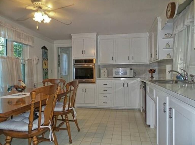 A kitchen with white cabinets, white floor tiles, and a wooden table and chairs on the left