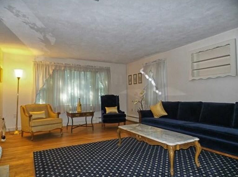 A living room with a blue velvet sofa and armchair, antique-style coffee table, white curtains and a large blue and white area rug