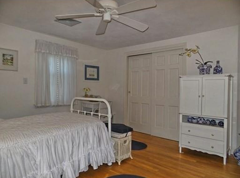 A bedroom with an old-fashioned iron bed, white wardrobe, short curtains in the window and white doors of a closet