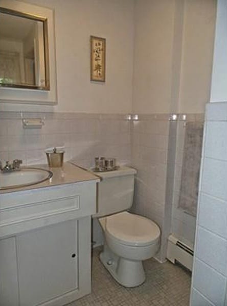 A sink and toilet in a bathroom with light grey ceramic tiles halfway up the walls 