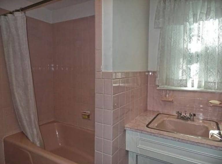A pink sink, pink tiles around tub and sink area and a window with lace curtains above pink and white sink
