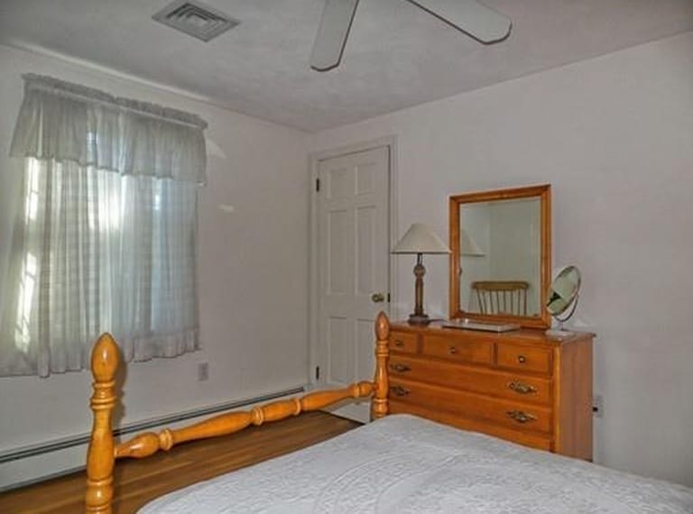A bedroom with old-fashioned bed, large oak dresser and mirror and a window with short, white curtains